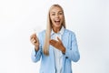 Smiling blond saleswoman pointing at credit card, demonstrating banking offer, standing in suit over white background