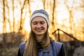 Smiling blond woman with closed in a knitted hat on the street against the backdrop of a golden sunset Royalty Free Stock Photo