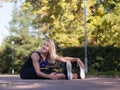 Smiling blond woman doing back stretching sitting on the pavement in urban park outdoor, selective focus Royalty Free Stock Photo