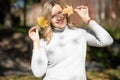 Smiling blond woman white sweater, holding golden foliage yellow leaves maples two hands,hiding face, blurred. Close up Royalty Free Stock Photo