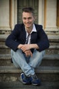 Smiling blond young man sitting on stone stair steps outside Royalty Free Stock Photo