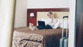 Smiling businesswoman in white shirt using on laptop and talking at mobile phone while lying on bed in hotel room Royalty Free Stock Photo