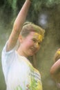 Smiling blonde caucasian teenage girl covered in green and yellow paint celebrates at the end of a charity Colour Paint Run.