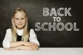 Smiling blonde child girl thinking on chalkboard. Back to school