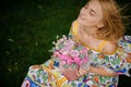 Smiling blonde girl with closed eyes sits on the lawn and holds round box with roses Royalty Free Stock Photo