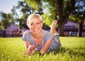 A smiling blonde girl with a short haircut is lying in a city park on green grass. A woman is resting in a park and looking into Royalty Free Stock Photo