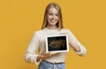 Smiling blonde girl showing tablet computer with modern blogging terms on screen, orange background. Collage