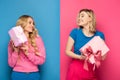 Blonde girls looking at each other while holding gift boxes on blue and pink background Royalty Free Stock Photo