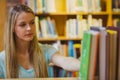 Smiling blonde picking out a book of bookshelves Royalty Free Stock Photo