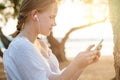 Smiling blonde teenage girl in headphones holding mobile phone and standing sideways on the background of sea Royalty Free Stock Photo