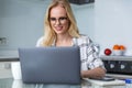 Smiling blonde woman in eyeglasses using laptop while working