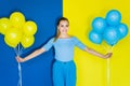 Smiling blonde woman holding blue and yellow balloons on blue