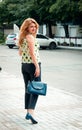 Smiling blonde woman with long hair in pants and blouse holding blue bag