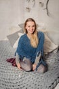 Smiling blonde woman sitting on the grey knighted bed cover. Royalty Free Stock Photo