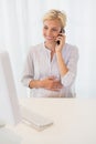 Smiling blonde woman using computer and phoning Royalty Free Stock Photo