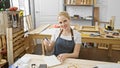A smiling blonde woman in a workshop taking notes, surrounded by carpentry tools, embodying craftsmanship and creativity Royalty Free Stock Photo