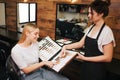 Smiling blonde young woman and hairdresser choosing hair color from palette before coloring in beauty salon. Beauty