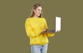 Smiling blondy woman in casual yellow sweatshirt and jeans working on laptop on khaki background.