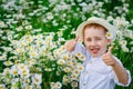 Smiling blue-eyed boy in a hat in a field of daisies, close-up portrait. Shows thumbs up Royalty Free Stock Photo