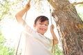 Smiling boy on the background of the sun and nature in a white T-shirt on a swing Royalty Free Stock Photo