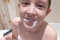 Smiling boy in the bathroom with a toothpaste around his mouth and inflating a toothpaste bubble