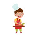 Smiling Boy Character in Hat and Apron Standing at Kitchen Table and Chopping Carrot Vector Illustration