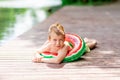 A smiling boy with a circle in the form of a watermelon lies on the lake in summer, a child`s rest in the village, a happy Royalty Free Stock Photo