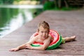 A smiling boy with a circle in the form of a watermelon lies on the lake in summer, a child`s rest in the village, a happy Royalty Free Stock Photo