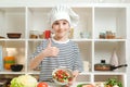 Smiling boy cooking healthy food and showing thumb up. Cute little boy wearing chef hat and uniform