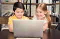 Smiling boy and girl sitting at table and using laptop together Royalty Free Stock Photo