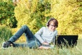 Smiling boy in glasses lying on lawn in front of laptop with headphones, looking at screen and enjoying online study. Royalty Free Stock Photo