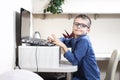 Smiling boy with glasses dressed in a blue shirt is sitting at a desk in front of a laptop. Royalty Free Stock Photo