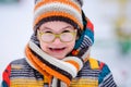 Smiling boy with green big glasses, knitting hat and scarf. Winter snowy background Royalty Free Stock Photo