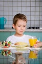 Smiling boy having dinner at the table and takes a glass of oran Royalty Free Stock Photo