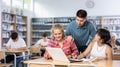 Smiling boy helping positive pupils research, working with laptop in library Royalty Free Stock Photo