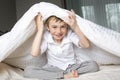 Smiling boy hiding in bed under a white blanket or coverlet. Royalty Free Stock Photo