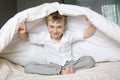 Smiling boy hiding in bed under a white blanket or coverlet. Royalty Free Stock Photo