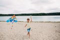 Smiling boy with a kite in his hands runs along the sandy beach on the banks of a picturesque river Royalty Free Stock Photo