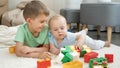 Smiling boy looking at his baby brother playing with toy bricks and blocks on floor at playroom Royalty Free Stock Photo