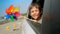 Smiling boy looking through open car window and holding colorful spinning pinwheel because of blowing wind. Concept of children Royalty Free Stock Photo