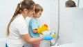 Smiling boy with mother washing bath and water sink. Children helping adults in housework and home cleanup.