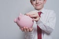 Smiling boy puts a coin in a pink piggy bank. Business concept. Black background Royalty Free Stock Photo