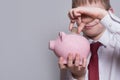 Smiling boy puts a coin in a pink piggy bank. Business concept. Light background Royalty Free Stock Photo