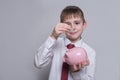 Smiling boy puts a coin in a pink piggy bank. Business concept. Light background Royalty Free Stock Photo