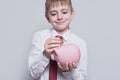 Smiling boy puts a coin in a pink piggy bank. Business concept. Light background Royalty Free Stock Photo