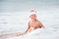 Smiling boy in Santa`s hat swims on ocean surfline. Christamas a Royalty Free Stock Photo