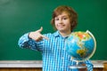 Smiling boy showing on globe over blackboard background . Educational and school concept. Royalty Free Stock Photo