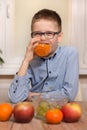 Smiling boy sits at the table and drinks juice from a glass. Tangerine, apples and grapes lie on the table.