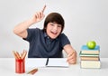 Smiling boy sitting at the desk raising hand with index finger to answer the question in the classroom Royalty Free Stock Photo