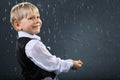 Smiling boy stands in rain and catches drops